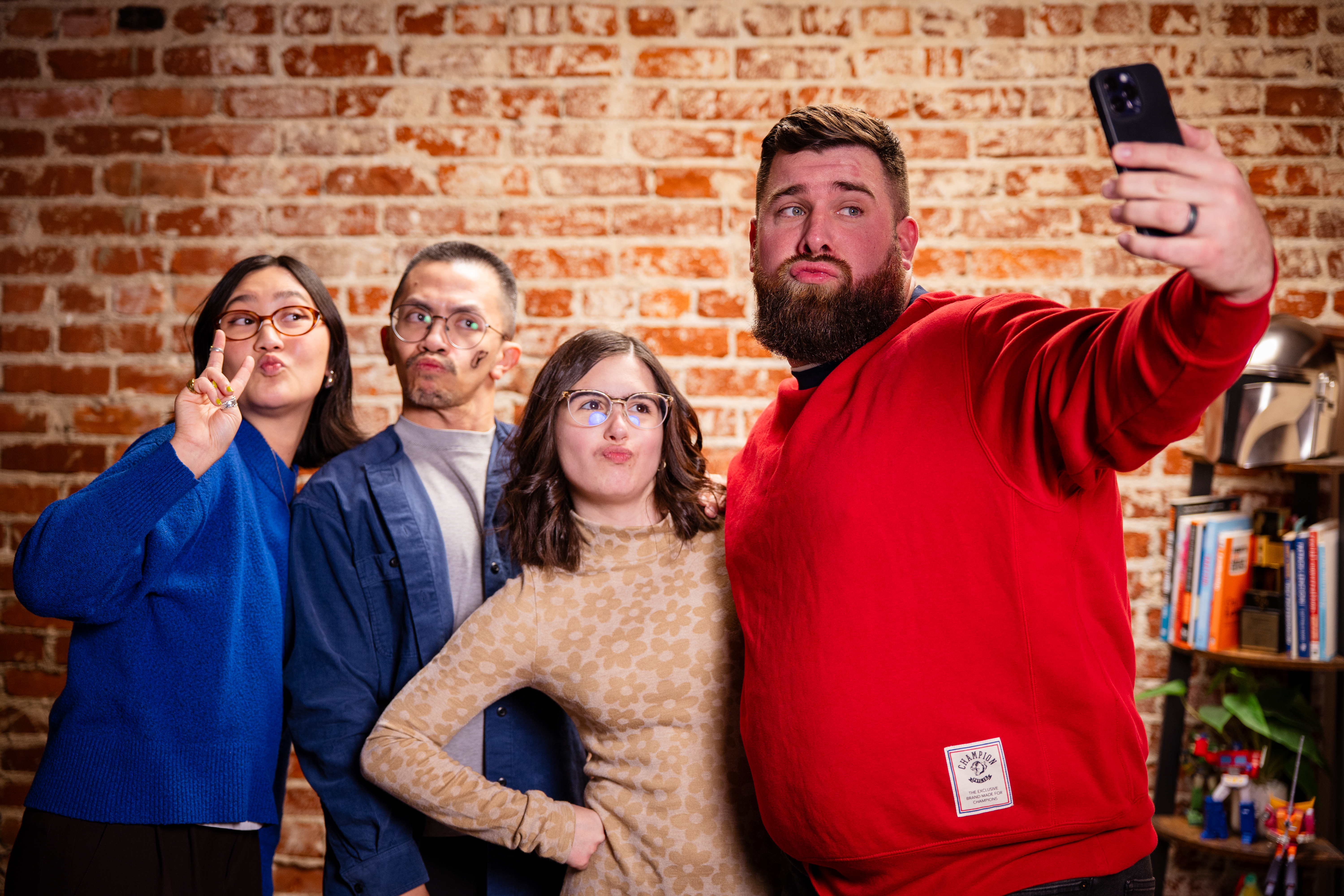 Group taking a selfie, casual pose, brick wall background.