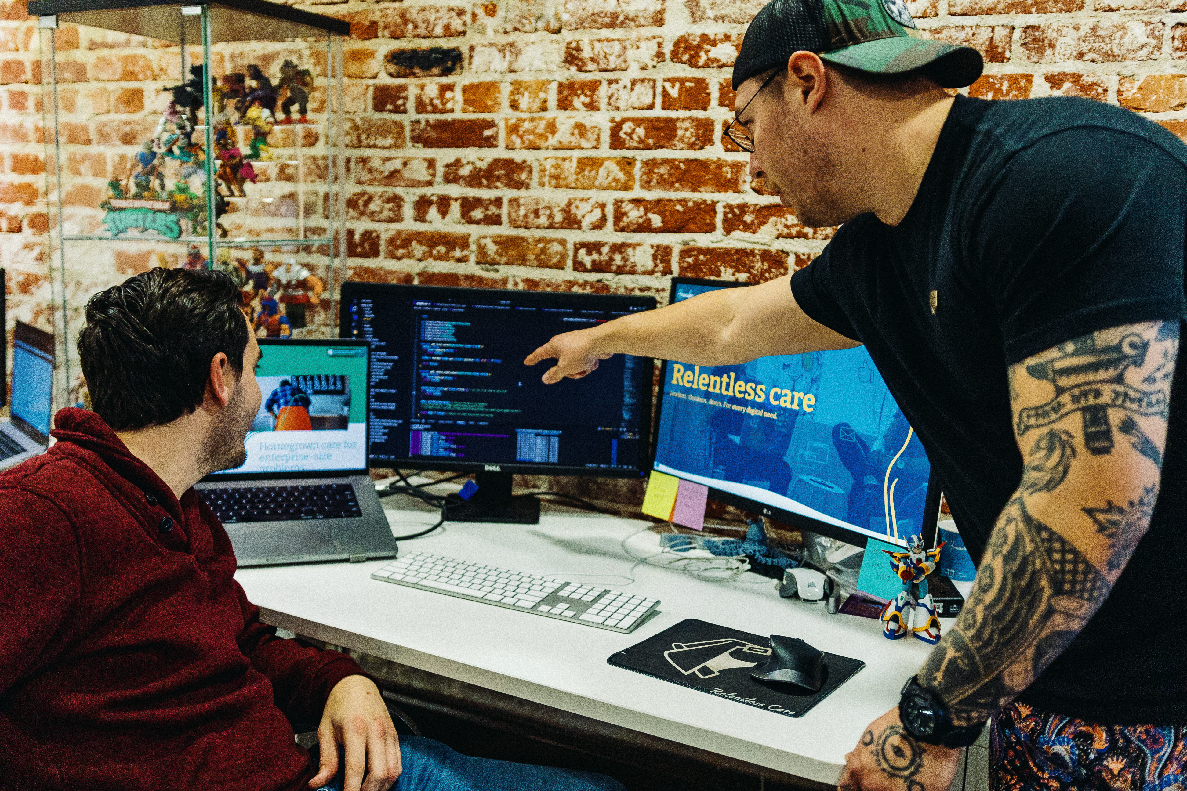 Two men collaborate in a tech office with computers displaying code.