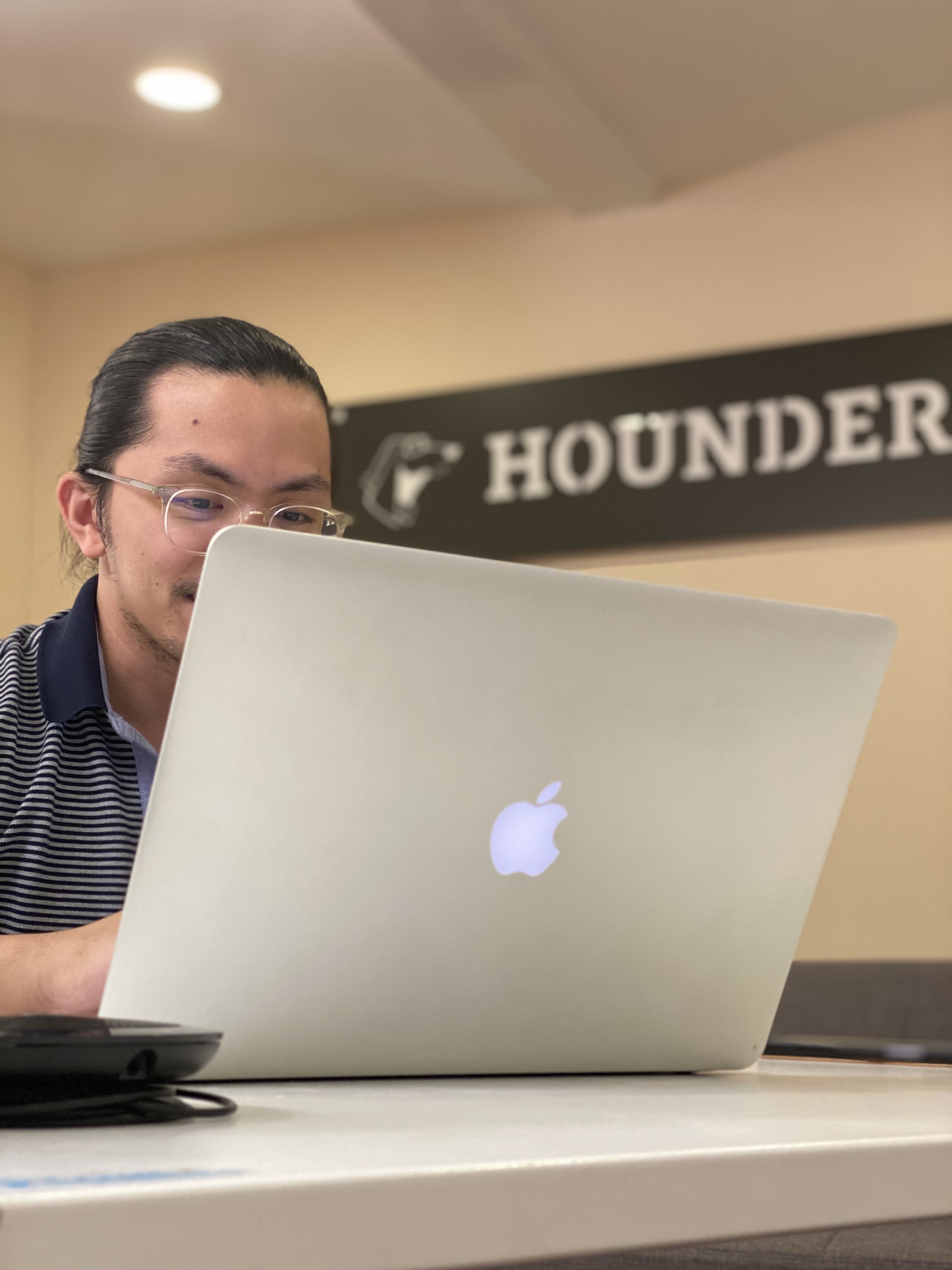 Person working on a laptop in front of a sign labeled "Hounder."