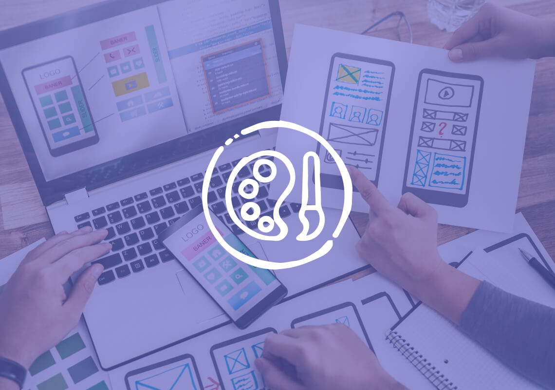 Hand holding mobile app wireframe sketch in front of a laptop showing digital design.