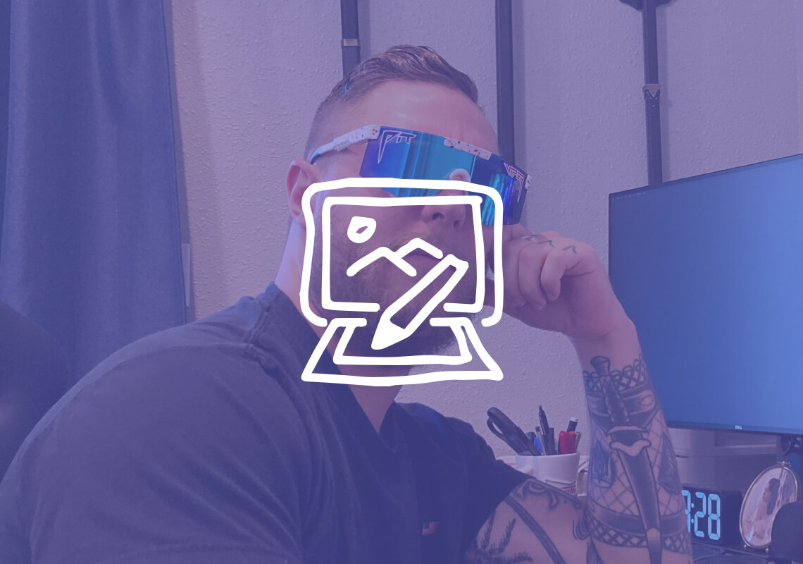 Man with a beard wearing reflective sunglasses indoors near a computer screen.