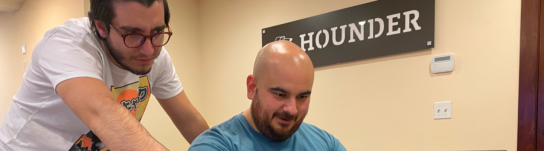 Two men collaborating on a project in an office setting with a Hounder sign.