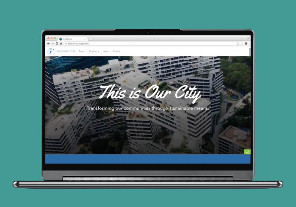 Laptop displaying "This is Our City" website with cityscape background.