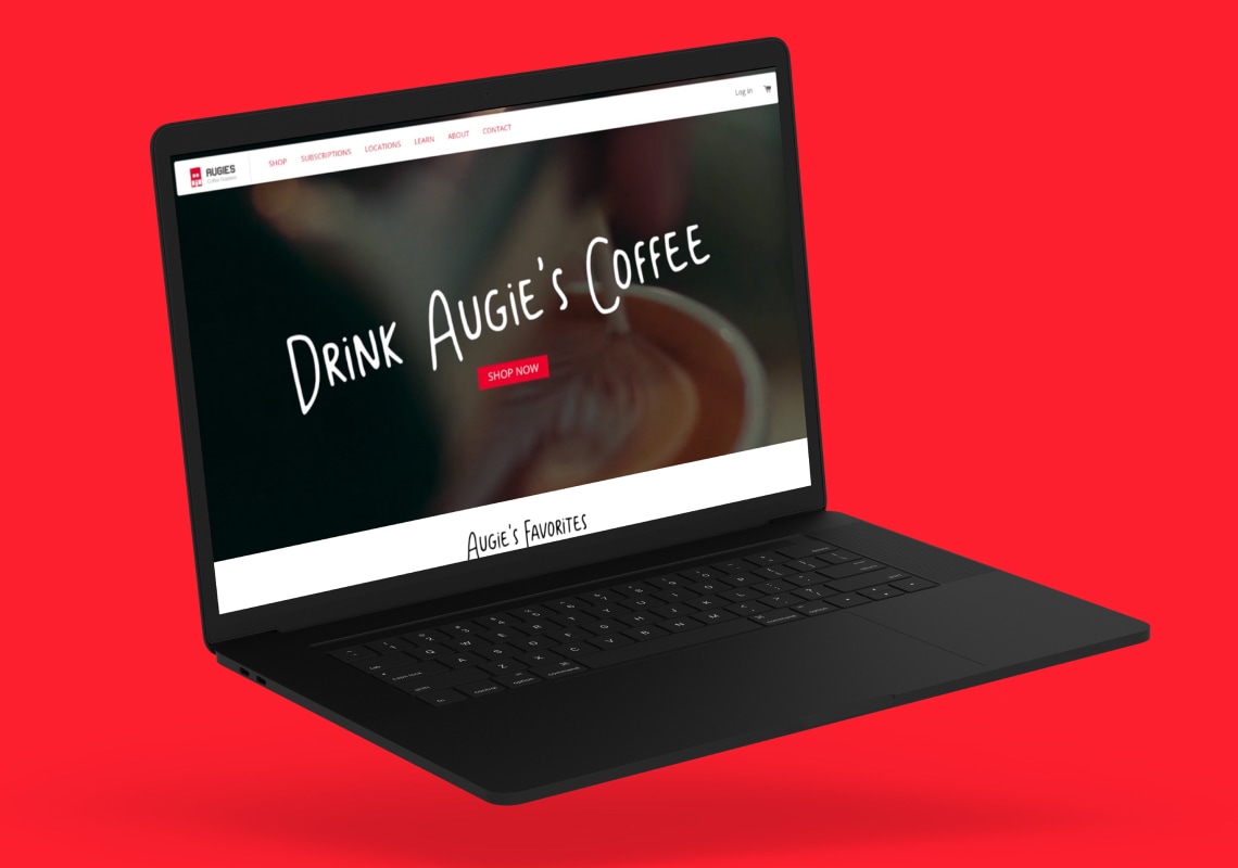 Black laptop displaying Augie's Coffee website on a red background.