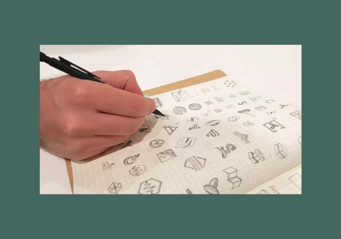 Hand sketching various logo designs on graph paper.