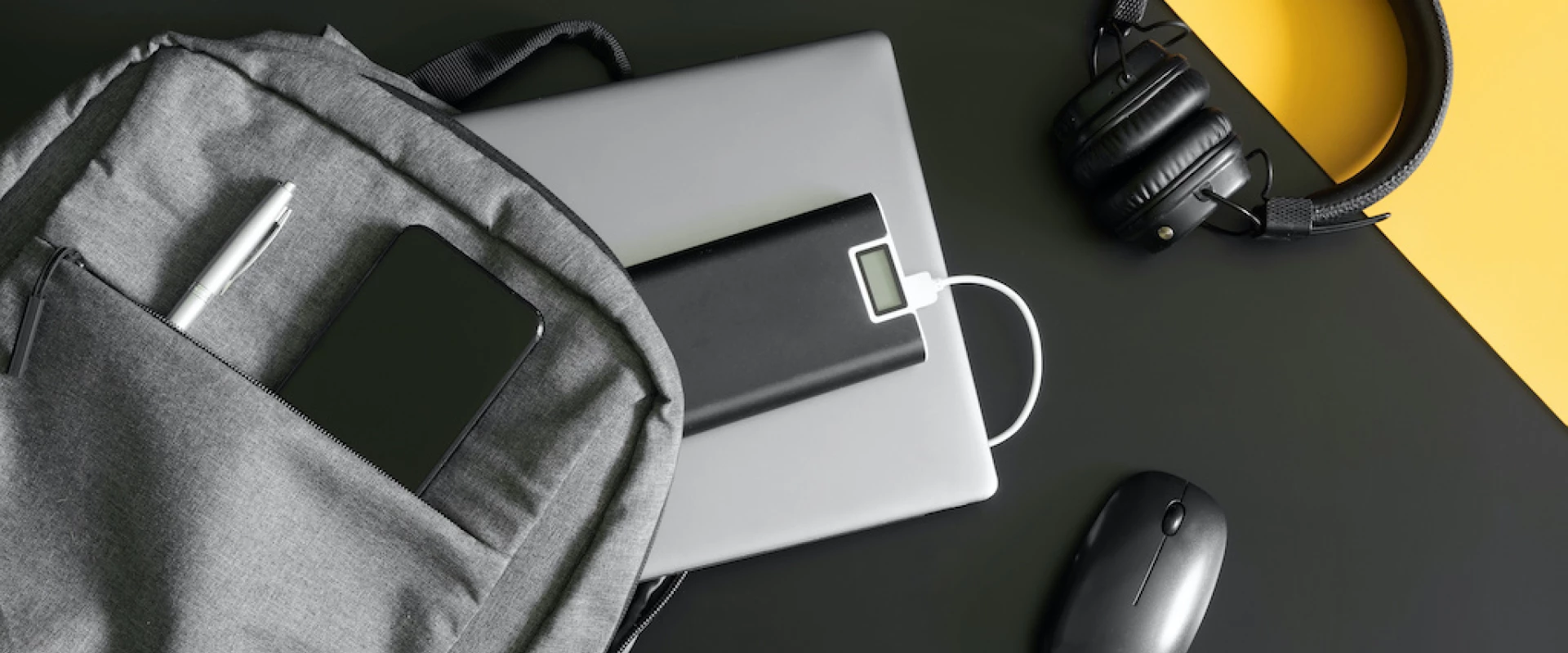 Backpack with laptop, headphones, smartphone, and power bank on a desk.