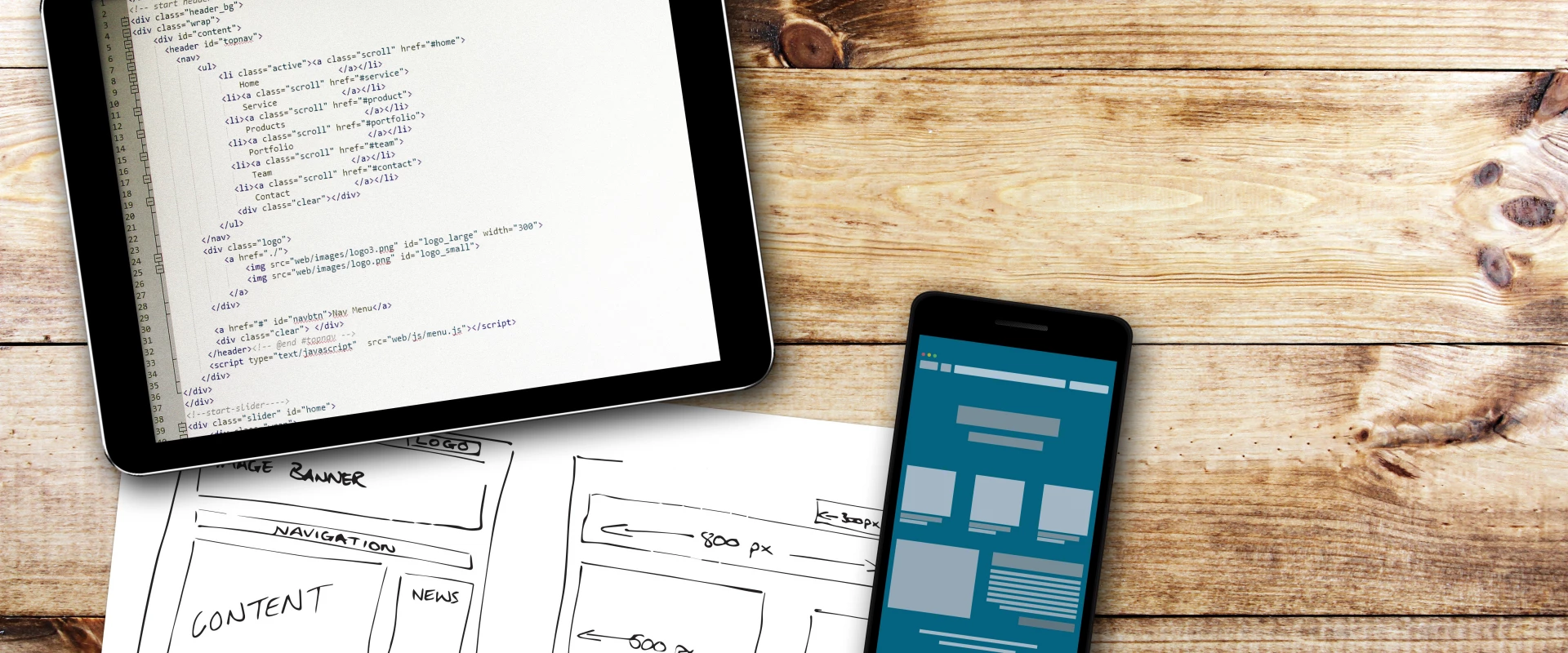 Tablet and smartphone with code and web design sketches on wood desk.