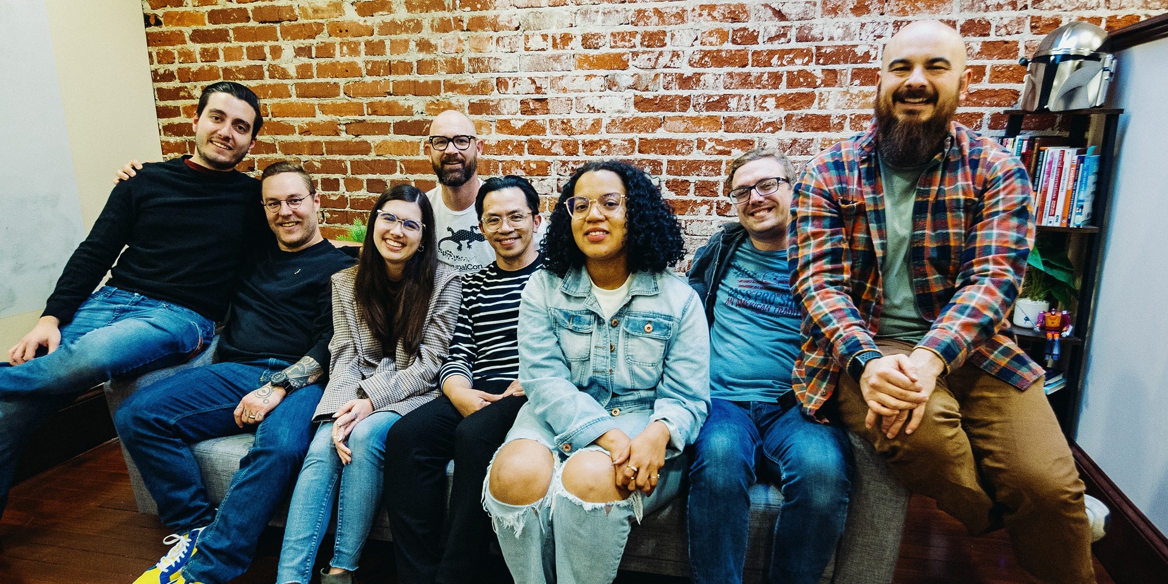 Group of people smiling while sitting on a couch in front of a brick wall.