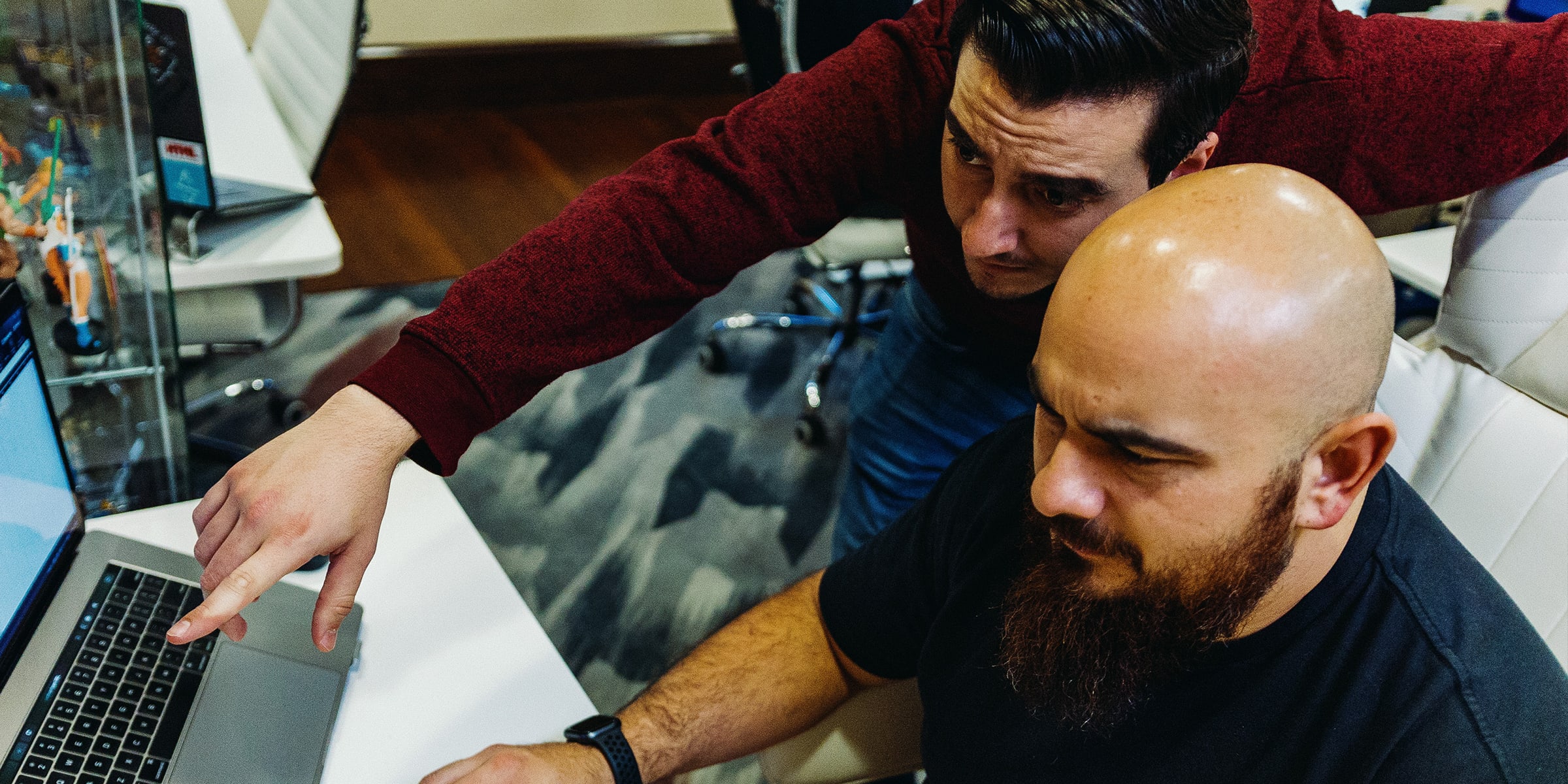 Two men collaborate on a laptop in a modern office setting.