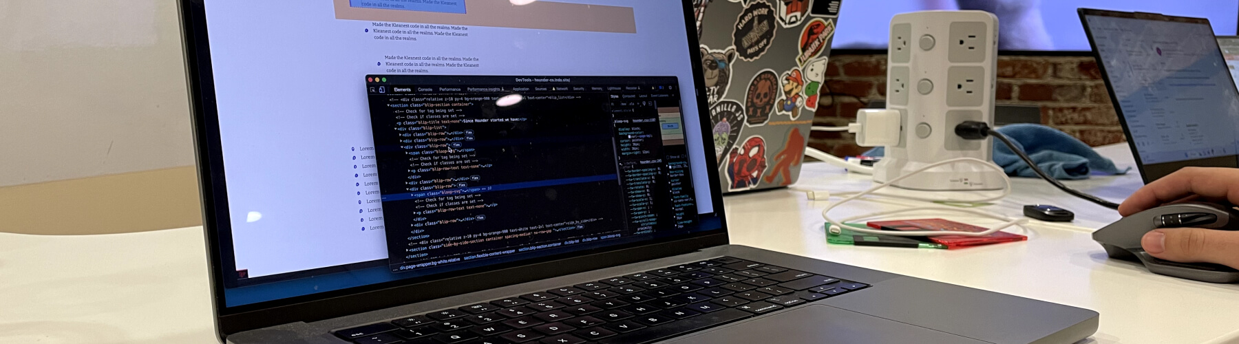 Laptop displaying code editor on desk, person using mouse.
