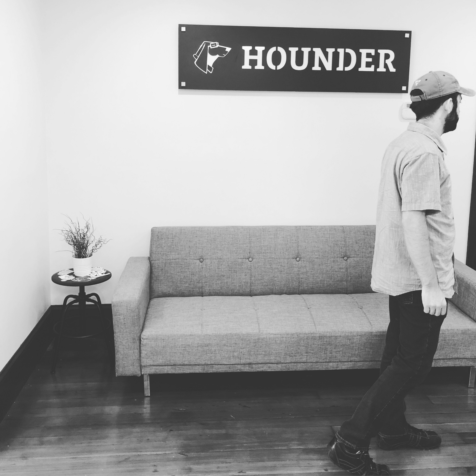 Man walking in a minimalist office with Hounder sign, sofa, and side table.