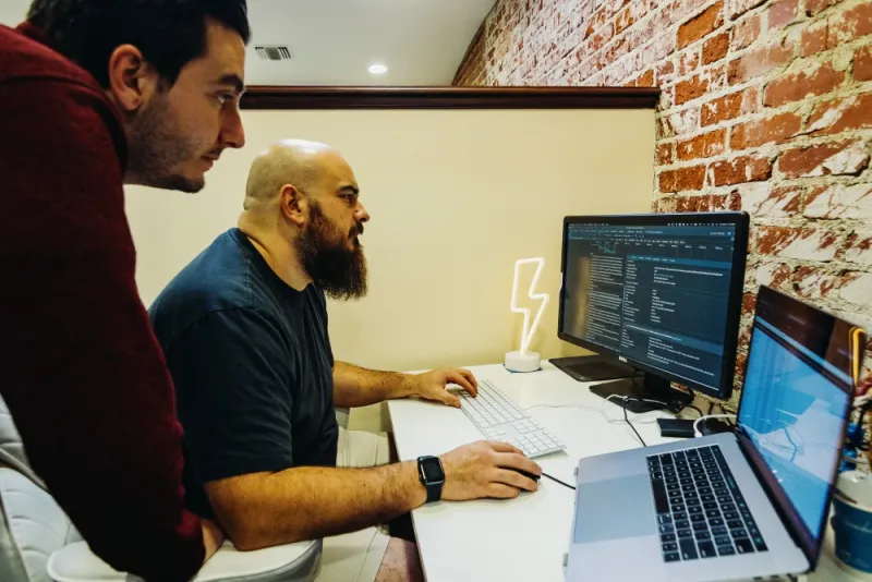 two employees at a desk working on code for a website