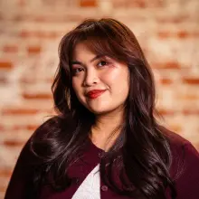 Smiling woman with long hair against a brick wall background.