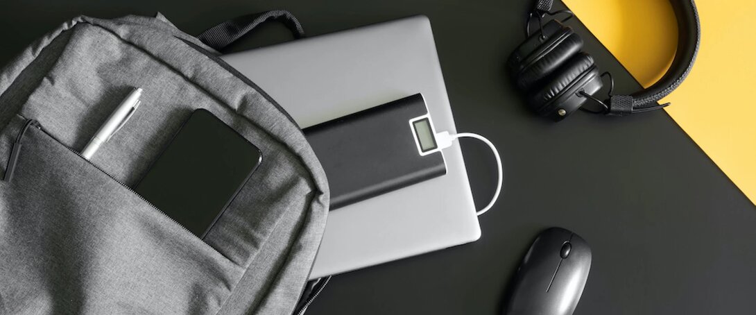 Laptop, headphones, power bank, and backpack essentials on a black and yellow surface.