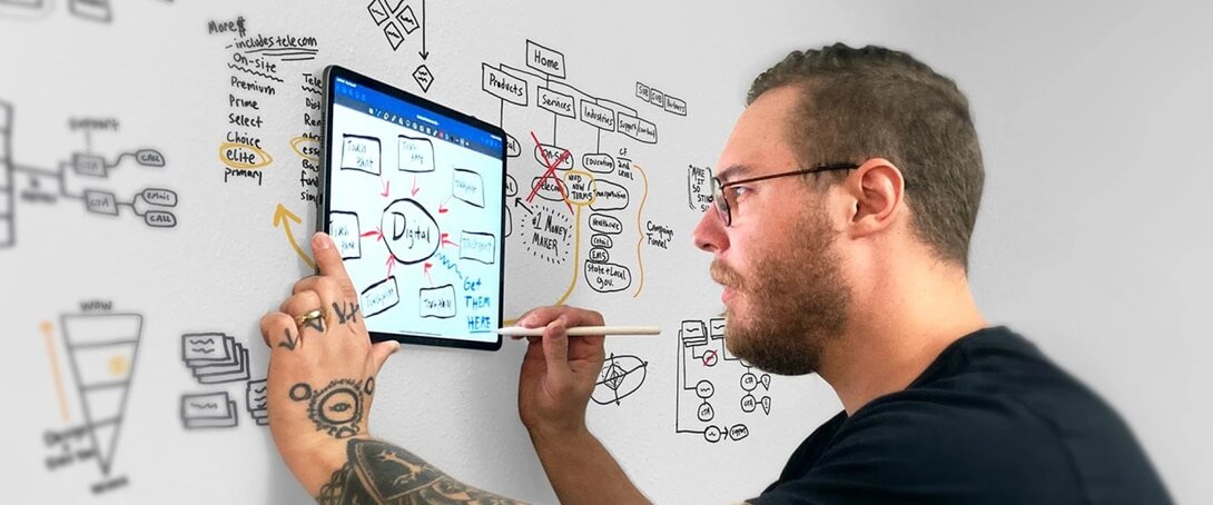 Man brainstorming digital ideas on a glass board with tablet and stylus.
