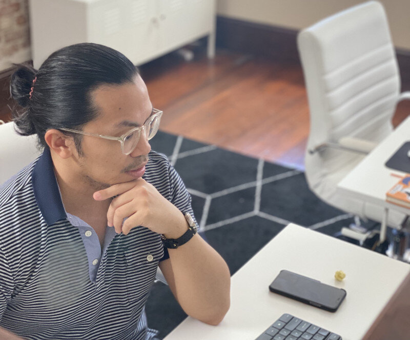 Man in striped shirt thinking at a desk in a modern office setting.