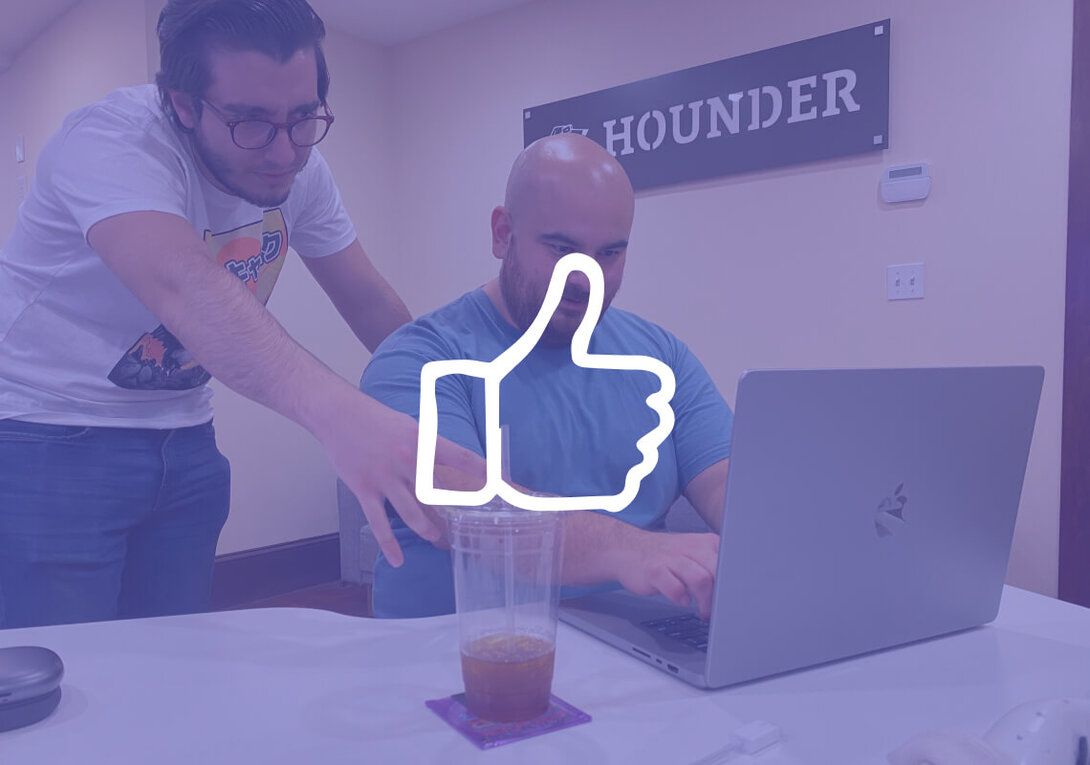 Two men working on a laptop with a thumbs-up overlay in an office setting.