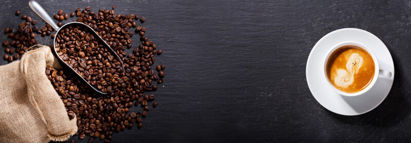 Coffee beans with scoop and espresso cup on dark surface.