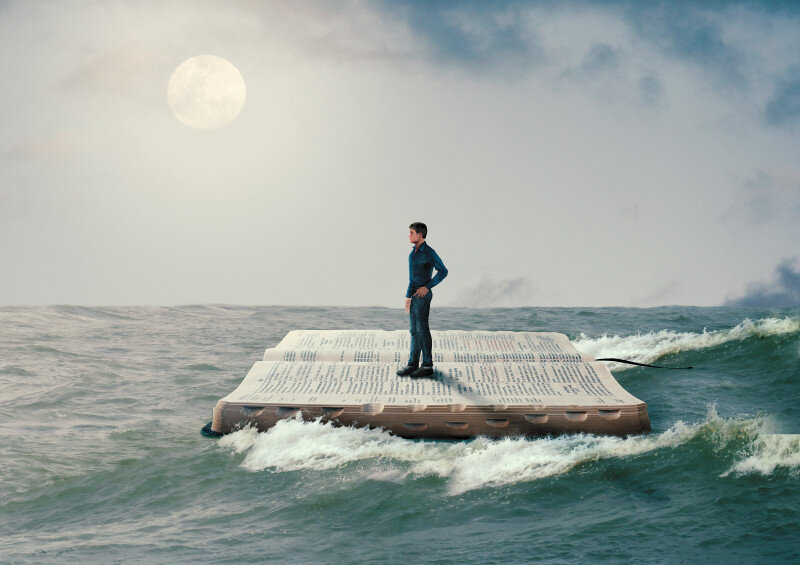 Man stands on giant floating book in ocean under full moon.
