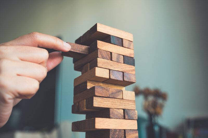 Hand carefully removing a block from a wooden tower game.