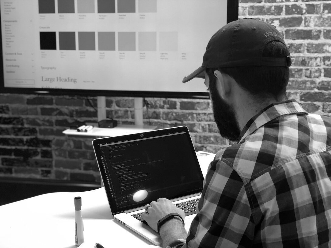Man coding on a laptop in a modern office with design prototypes on the screen.