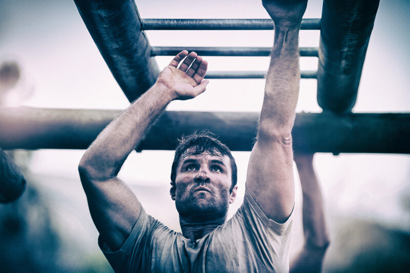 Determined man climbing monkey bars during outdoor obstacle course.