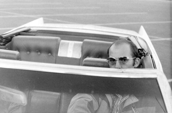 Man wearing sunglasses driving a vintage convertible car, partial view.