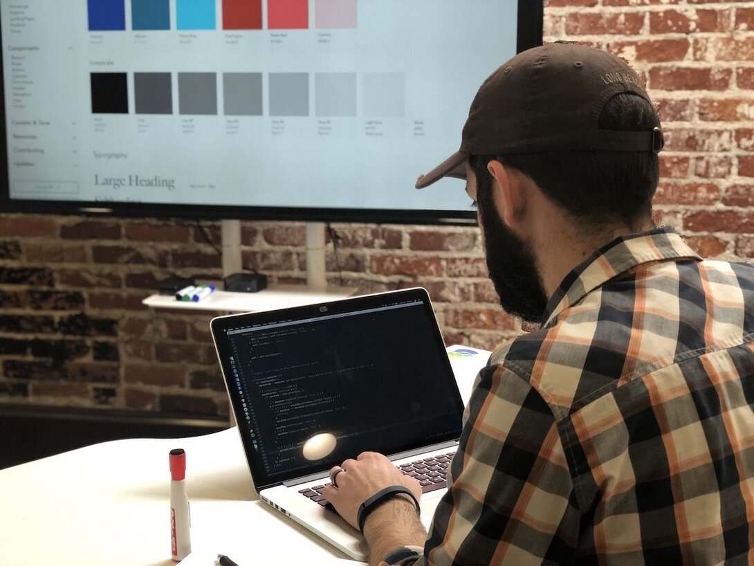 Developer working on a laptop with design elements displayed on the screen in a modern office.