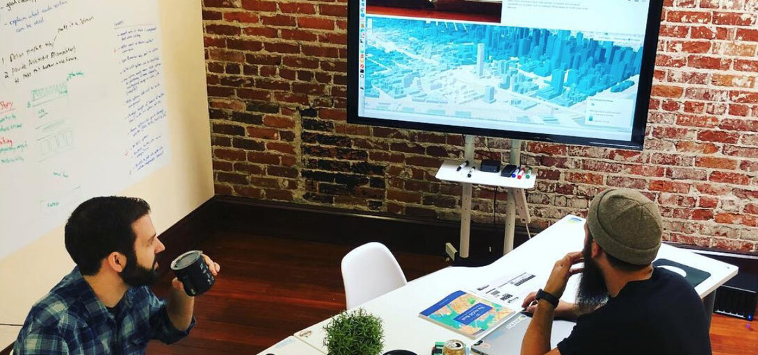 Two men collaborate in a modern office with a digital map on the screen.